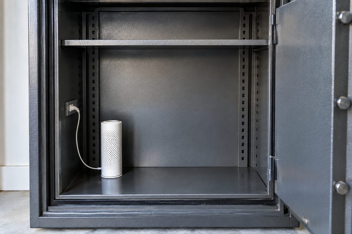 Inside an empty steel safe with a white cylinder-style electric dehumidifier on the bottom shelf, cord running to an outlet